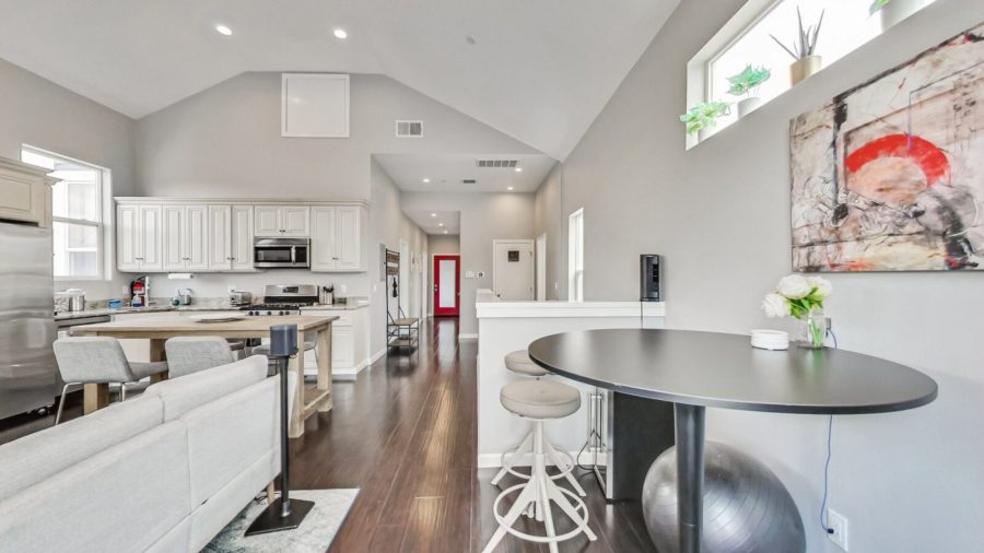 Open concept living room, dining room, and kitchen, hallway leads down to bedrooms, red door opens to the back deck.