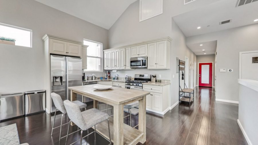 Open concept living room, dining room, and kitchen, hallway leads down to bedrooms, red door opens to the back deck.