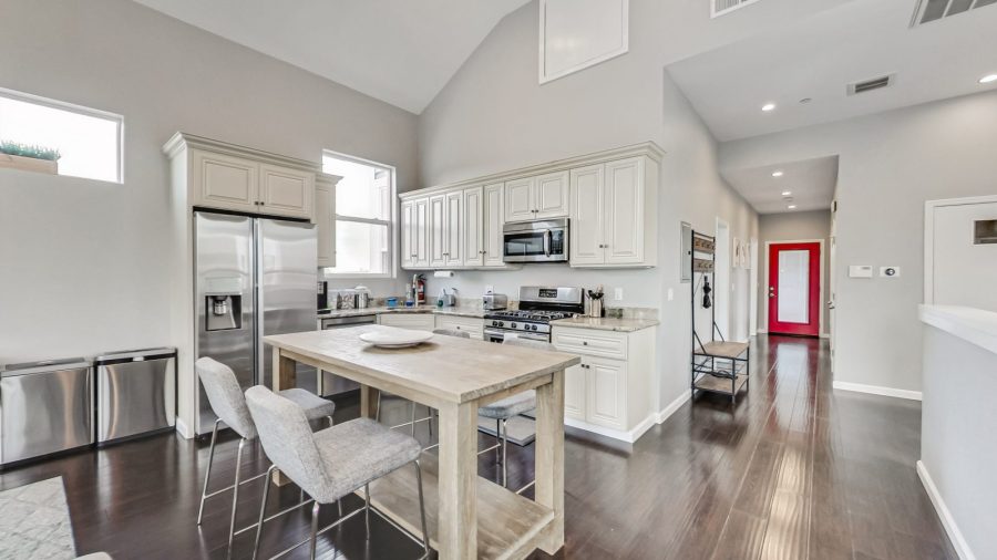 Open concept living room, dining room, and kitchen, hallway leads down to bedrooms, red door opens to the back deck.